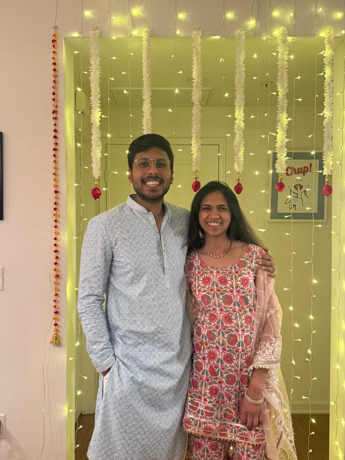 Aditi and Vedant in Indian traditional clothes in front of a curtain of fairy lights
